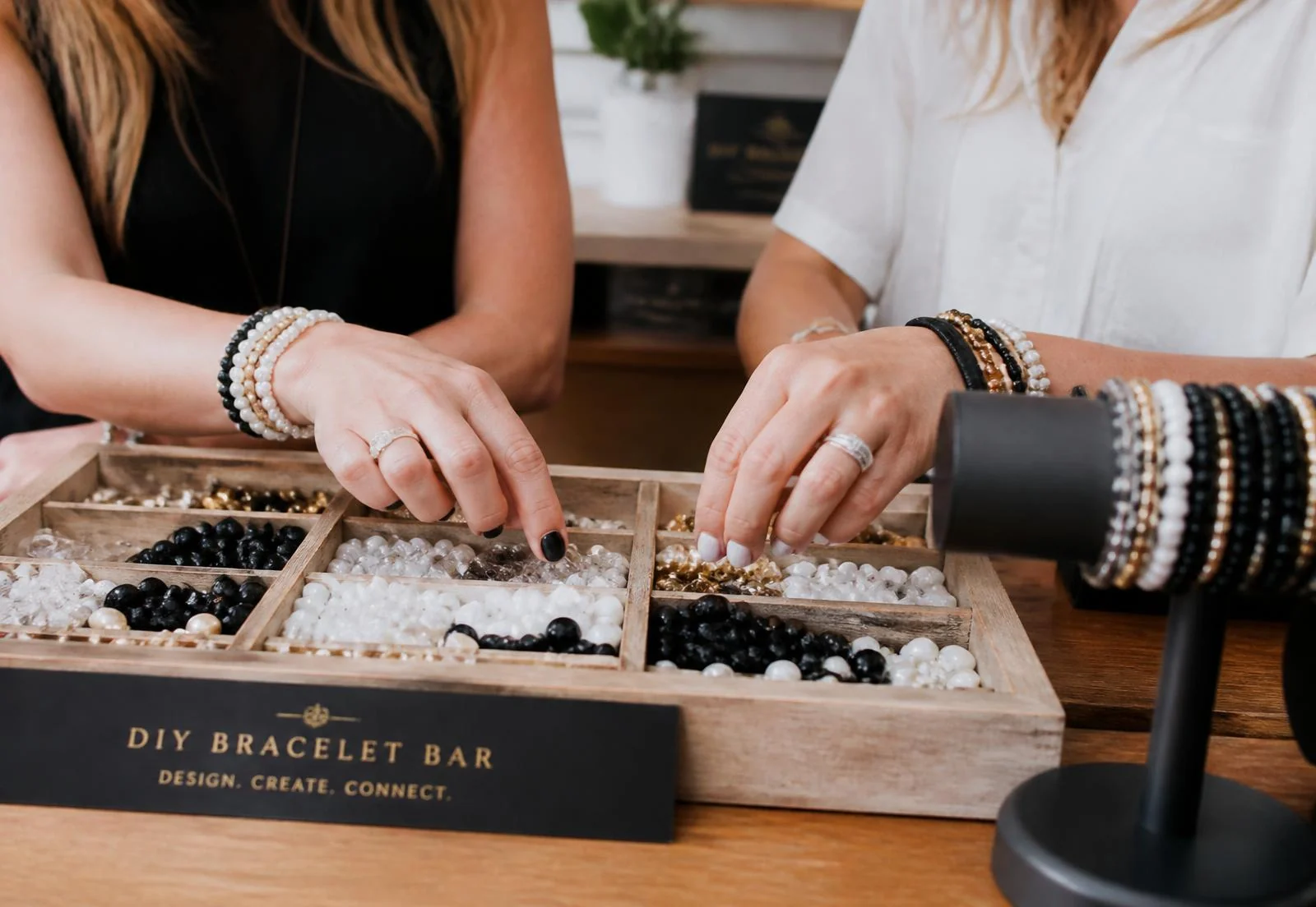 Hands choosing black, pearl and crystal beads from a wooden tray at the bracelet bar
